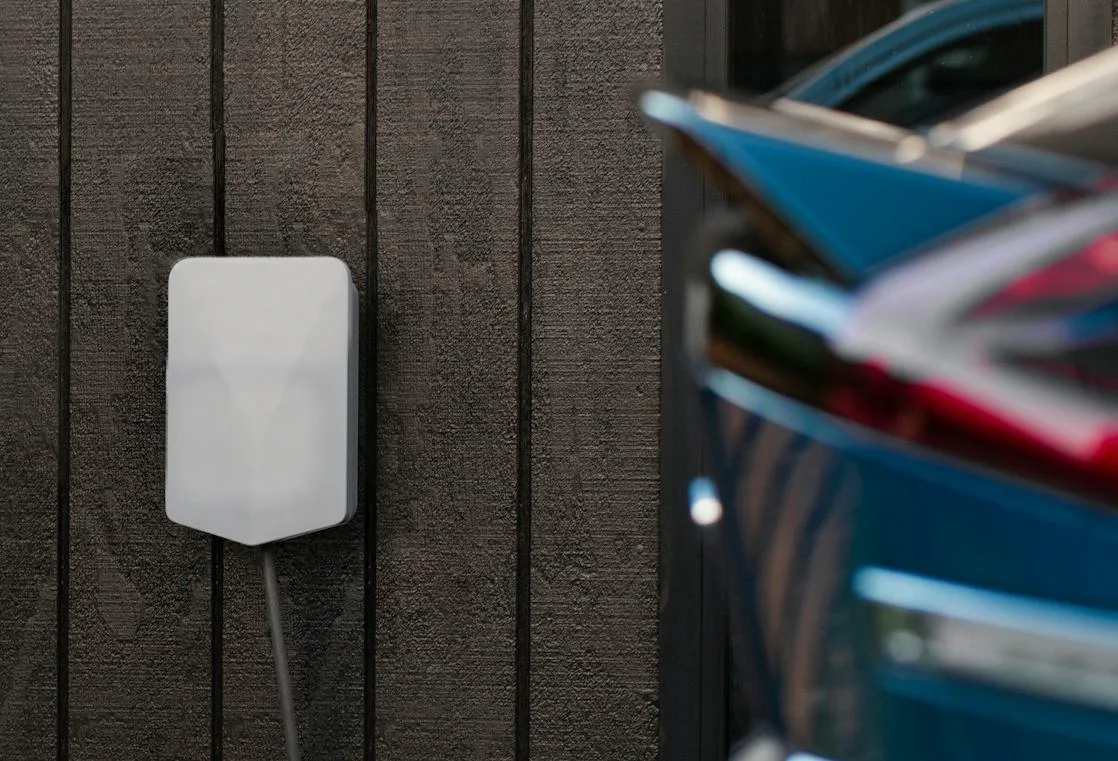 An electric car charging from a wall charger on a driveway